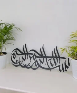 Premium black metal Arabic calligraphy wall art featuring the phrase ‘Bismillah-ir-Rahman-ir-Rahim’ elegantly displayed between two decorative indoor plants. Perfect for modern Islamic home decor and stylish interior design. best arabic calligraphy art